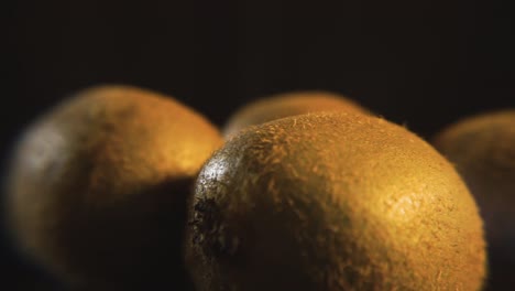 grupo de kiwis enteros girando frente a una pantalla negra, iluminados por luz de estudio profesional - imágenes macro