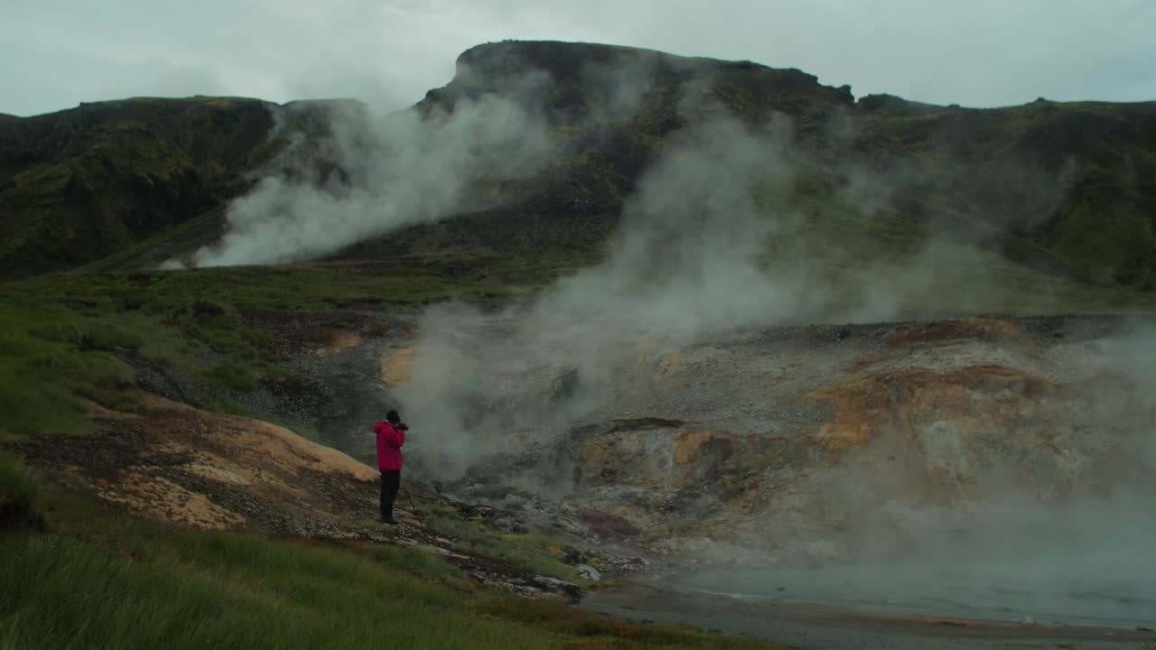 paisaje de islandia, humo de vapor de aguas termales geotérmicas, figura distante de un fotógrafo tomando una foto de una escena completa, tiro de gran angular