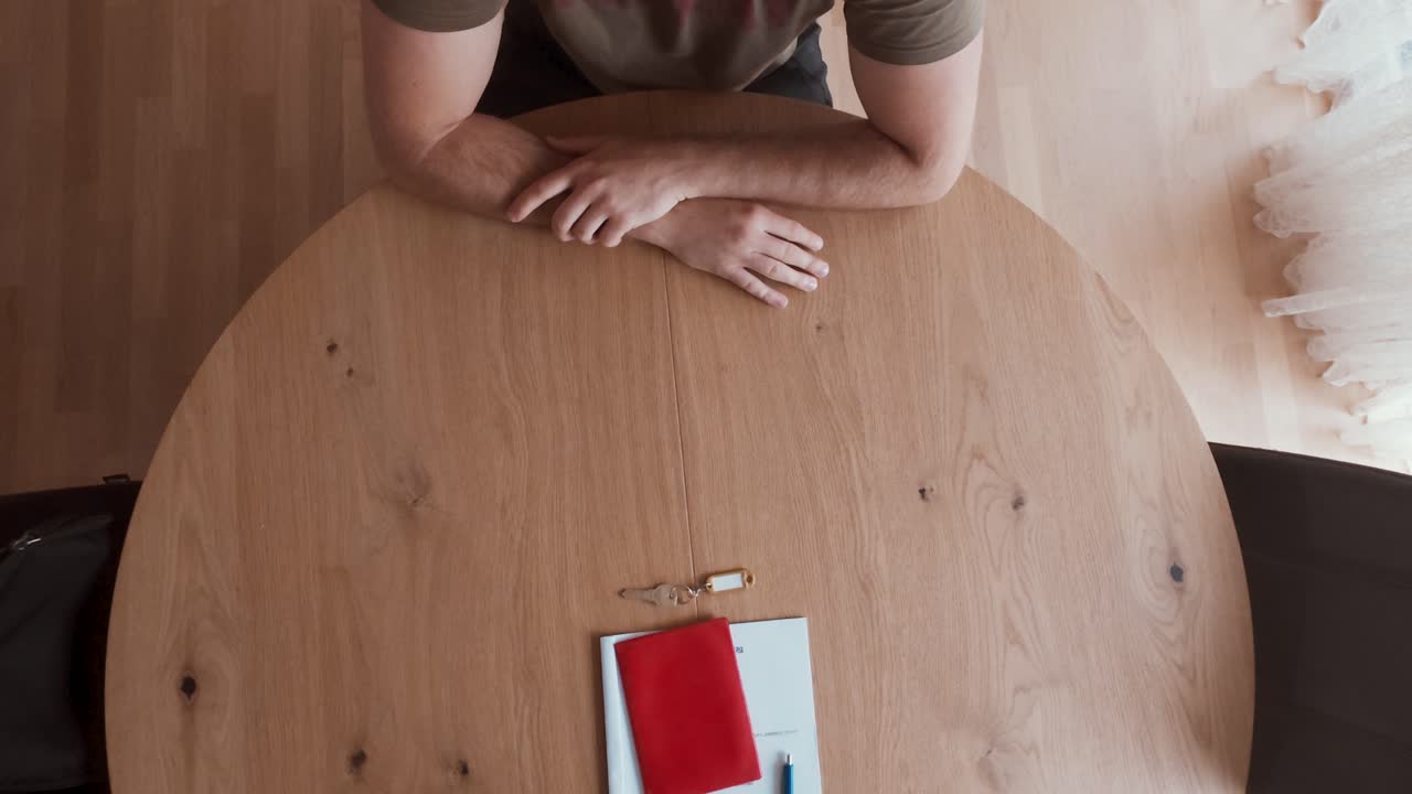 A man sits at a wooden table with documents, a red folder, and keys, symbolizing the final step of a property handover or signing. Ideal for real estate, leasing, and ownership agreement themes