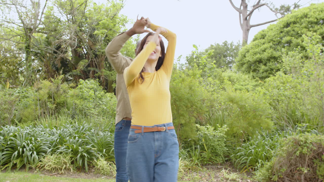 Diverse multiracial couple dancing joyfully in park, enjoying sunny day together
