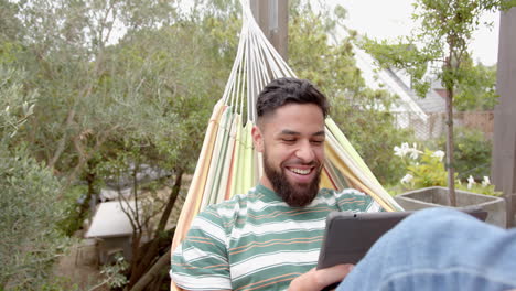 relaxing in hammock, man smiling and using tablet outdoors in backyard
