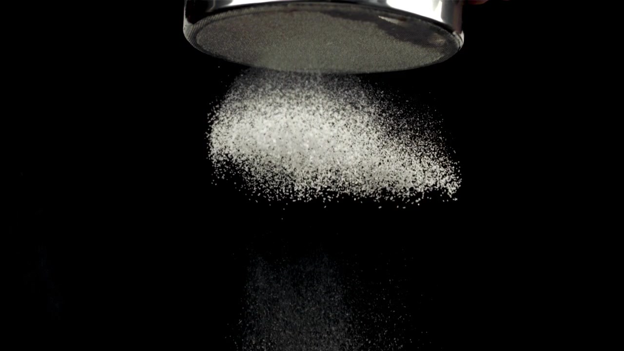 Polvo blanco cerniéndose a través de un tamiz sobre fondo negro.