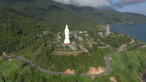 aerial drone flying towards tallest lady buddha statue and temples with huge mountains and ocean in da nang, vietnam