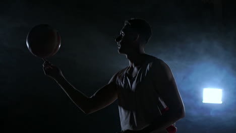 Close-footage-of-basketball-player-spinning-ball-on-his-finger,-dark-misty-room-with-floodlight