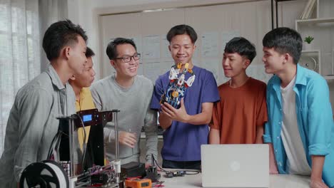 asian man with a laptop and 3d printing explaining about how to use a cyborg hand to the boys before celebrating the success at school