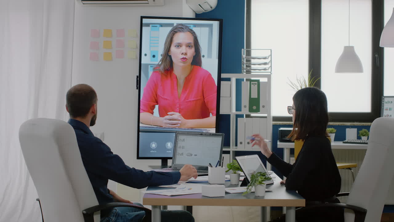 Workmates using video call on television for conversation with woman