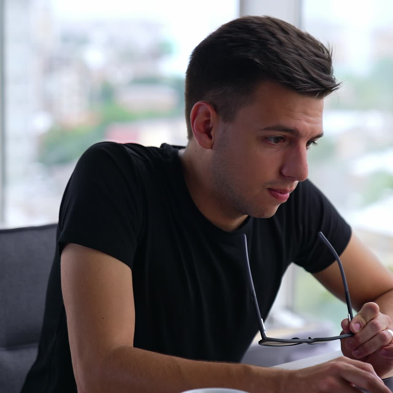 Un bell'uomo dai capelli scuri si toglie gli occhiali per guardare più da vicino lo schermo del computer. Freelancer che lavora al laptop in una grande stanza luminosa. Sfondo sfocato