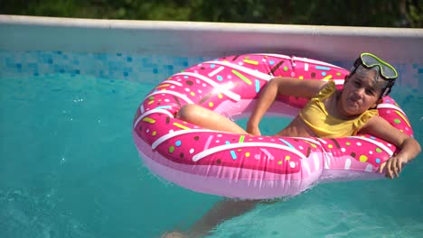 Süßes-Kleines-Mädchen-Im-Badeanzug,-Das-Auf-Einem-Aufblasbaren-Donut-Kreis-Liegt.-Das-Kind-Schwimmt-Auf-Blauem-Hintergrund