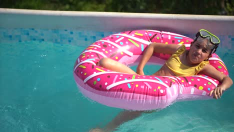 cute little girl in a bathing suit lying on a donut inflatable circle. the child swims on a blue background