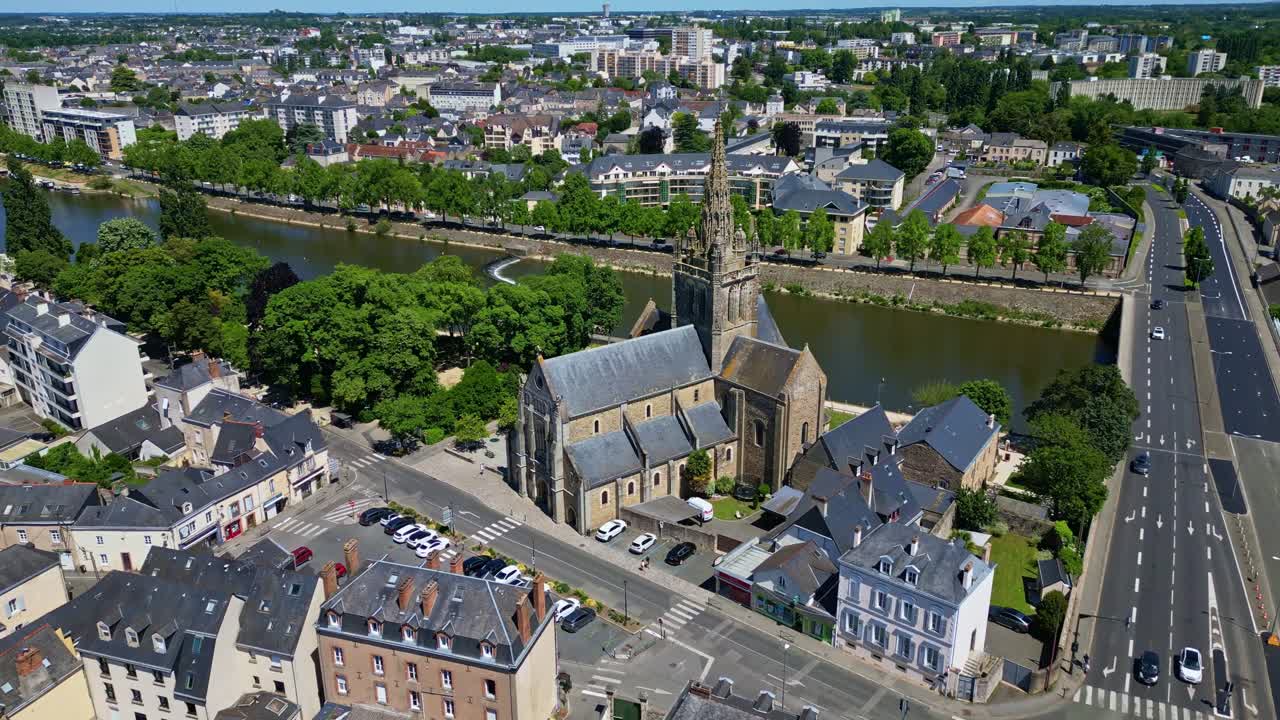 Drone flies forward past Avesnières Basilica showing Laval city, Mayenne River, trees on a sunny day. France