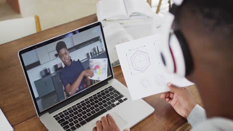 African-american-male-college-student-holding-notes-while-having-a-video-call-on-laptop-at-home