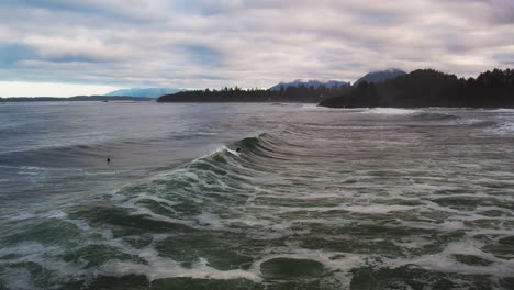 Two-surfers-catching-waves-off-Cox-Bay-beach-on-scenic-Tofino-coastline,-aerial