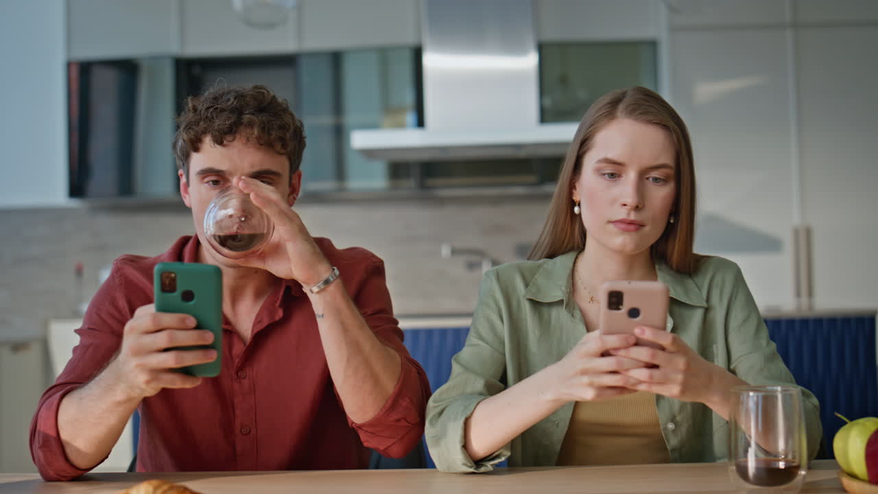 Serious couple using smartphones in kitchen at breakfast closeup. Young people