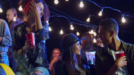 Happy-Joyful-Multiethnic-Group-Of-Young-Friends-Sitting-Chatting,-Joking-And-Laughing-At-Night-On-The-Rooftop-Party