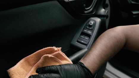 close up of a male wearing black gloves cleaning a white car with black interior with a microfiber cloth in slow motion