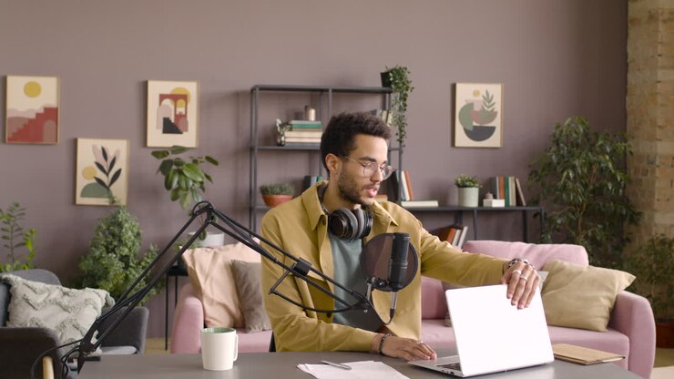 Mann öffnet einen Laptop und bereitet das Mikrofon vor, um einen Podcast aufzunehmen, während er an einem Tisch sitzt