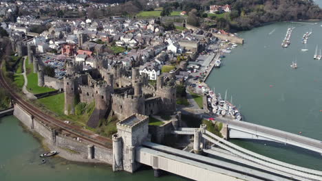 una vista aérea más amplia del castillo de conwy en un día soleado, volando de izquierda a derecha alrededor del castillo mientras se aleja con la ciudad al fondo, norte de gales, reino unido