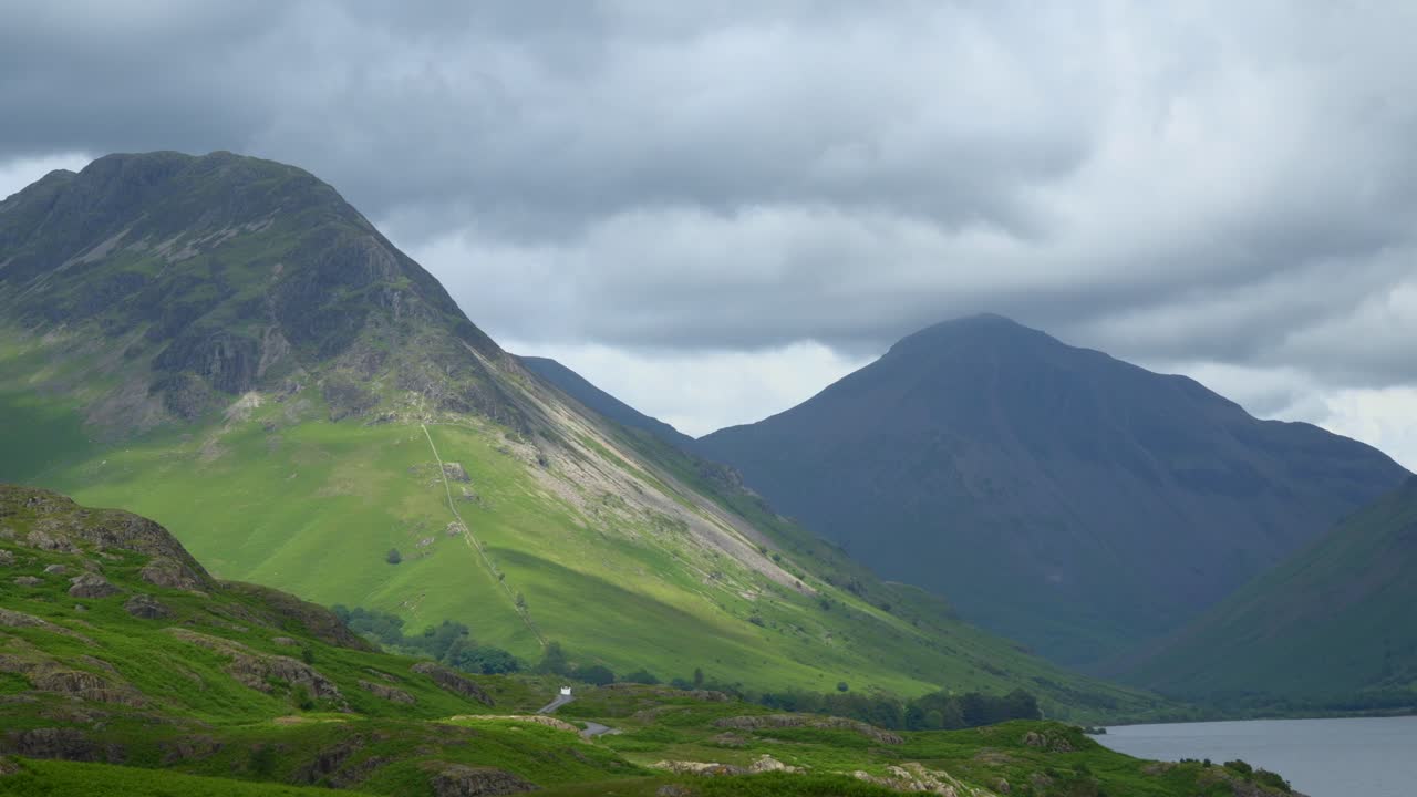 어두운 구름은 yewbarrow와 great gable의 산꼭대기를 고 구름 그림자는 호수  도로에서 가운 교통과 함께 풍경을 가로질러 달립니다.