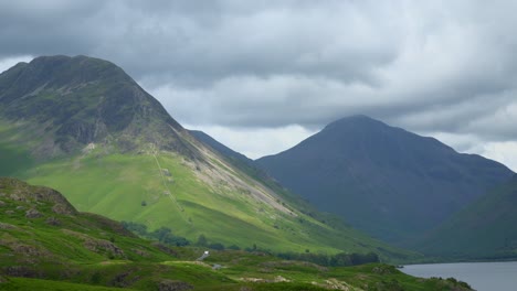 Dark-clouds-skimming-mountain-summits-of-Yewbarrow-and-Great-Gable-as-cloud-shadows-race-across-landscape-with-light-traffic-on-lakeside-road