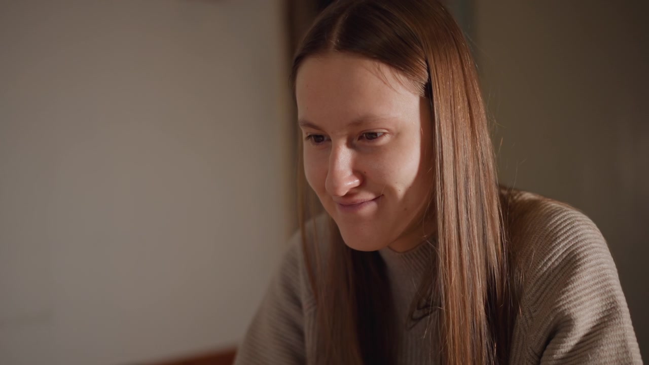 Caucasian woman quiet contemplation at desk soft warm light highlights long straight hair and wool sweater interior corner student reviewing notes writer drafting pages person pausing in thought