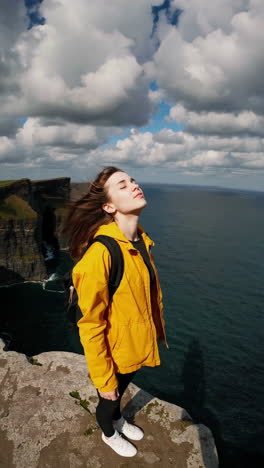 woman embracing the wind and views at the cliffs of moher, ireland