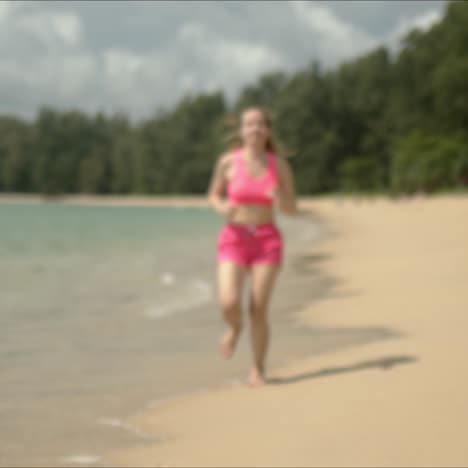 Pleasant-woman-in-pink-sweatsuit-running-on-beach