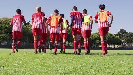 Video-of-diverse-group-of-male-football-players-warming-up-on-field,-running