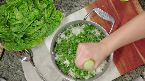 a hand squeezing lime juice over fresh cilantro and rice for a cooking process