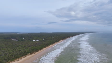 Der-Flug-Geht-Richtung-Norden-Zum-Rainbow-Beach-Mit-Ferienhäusern,-Die-Von-üppigen-Wäldern-Umgeben-Sind,-Während-Leichter-Nebel-Von-K&#39;gari-Fraser-Island-Herankommt