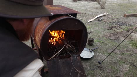 close up of a bushman loading firewood into a drum fire while camping in the australin desert