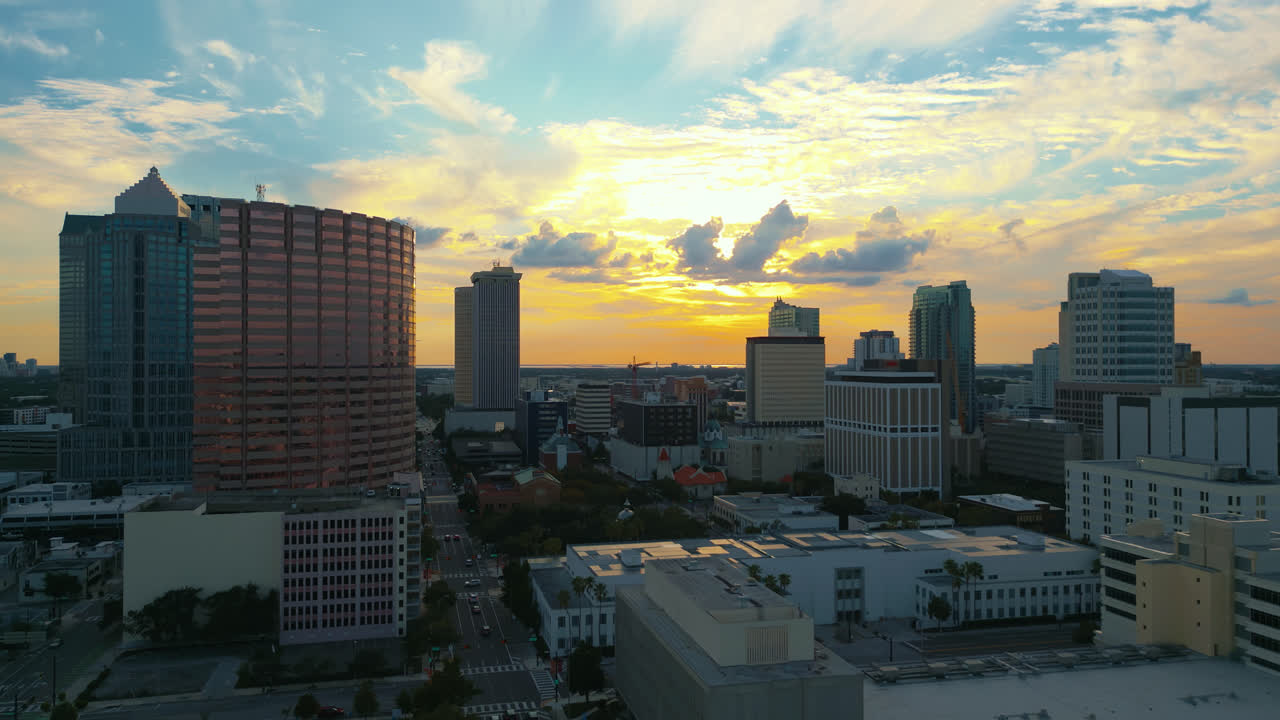Tampa skyline as the sun begins to set and beautiful colors fill the sky illuminating the clouds and traffic fills the streets, Aerial tracking left