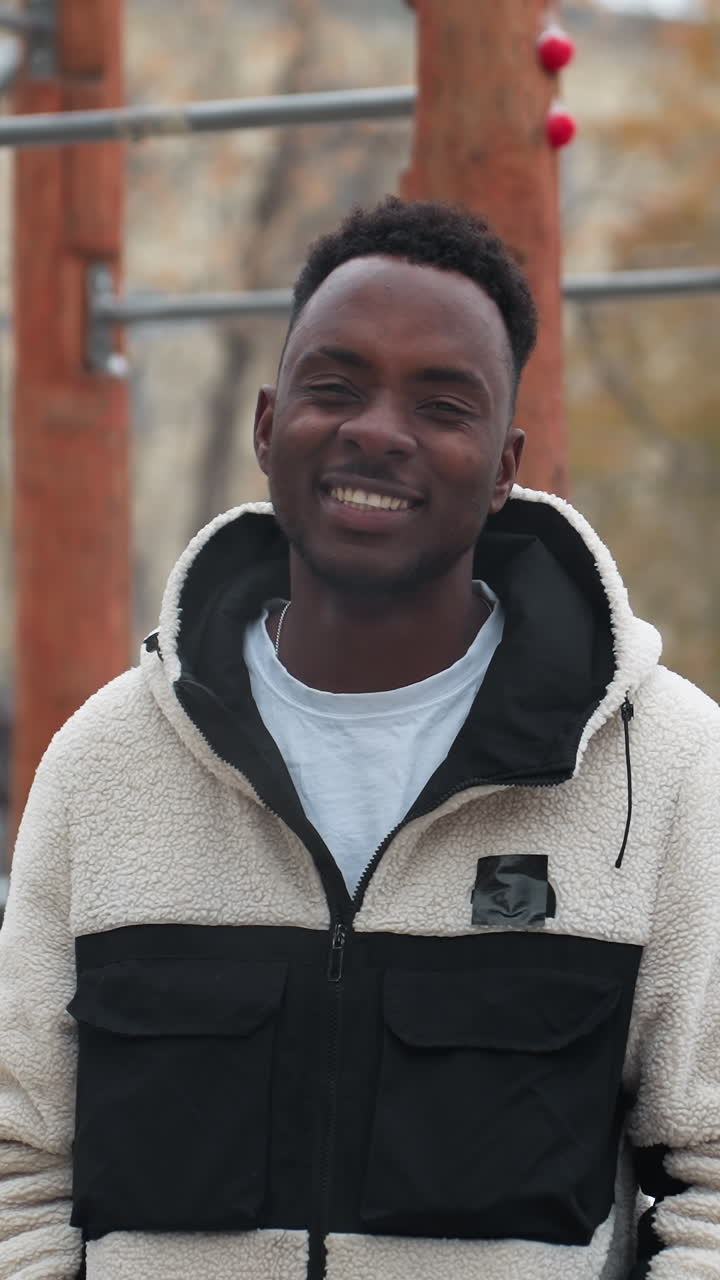 un alegre hombre africano con una cálida chaqueta de invierno se ríe mientras el aliento frío es visible en el aire frío. el suelo cubierto de nieve y los árboles desnudos crean una atmósfera de invierno pintoresca en un entorno urbano al aire libre