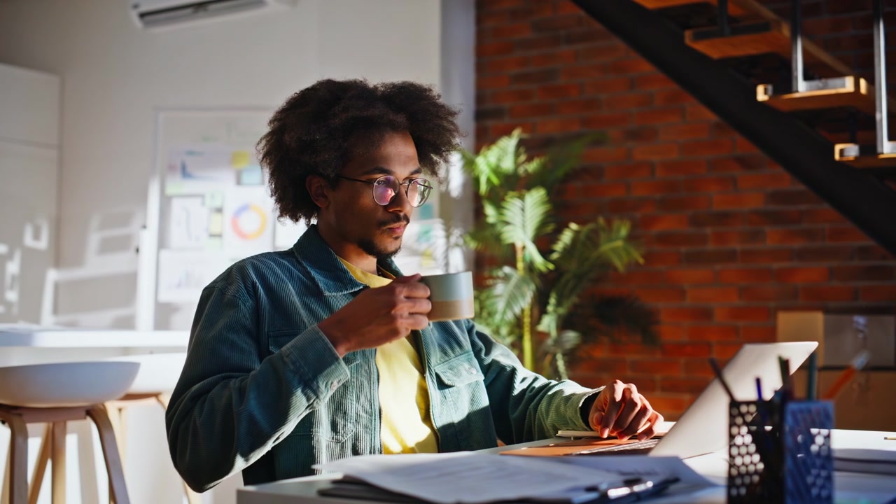 Giovane programmatore che digita al laptop bevendo caffè. Sviluppatore che lavora in un loft adibito a ufficio