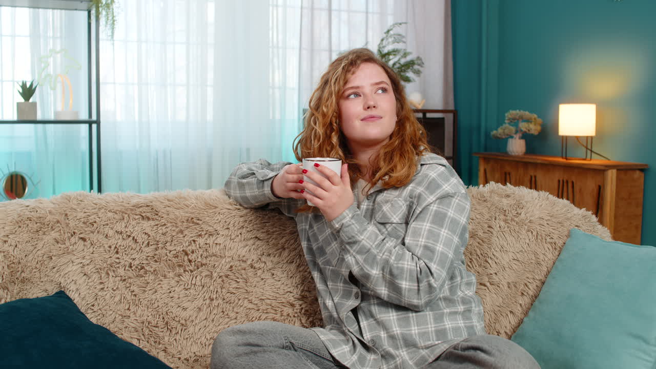 Woman sitting on sofa drinking tea with peaceful smile enjoying calm quiet rest and cozy relaxation