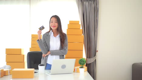 asian woman, small business owner in her office showing bank credit card looking at camera