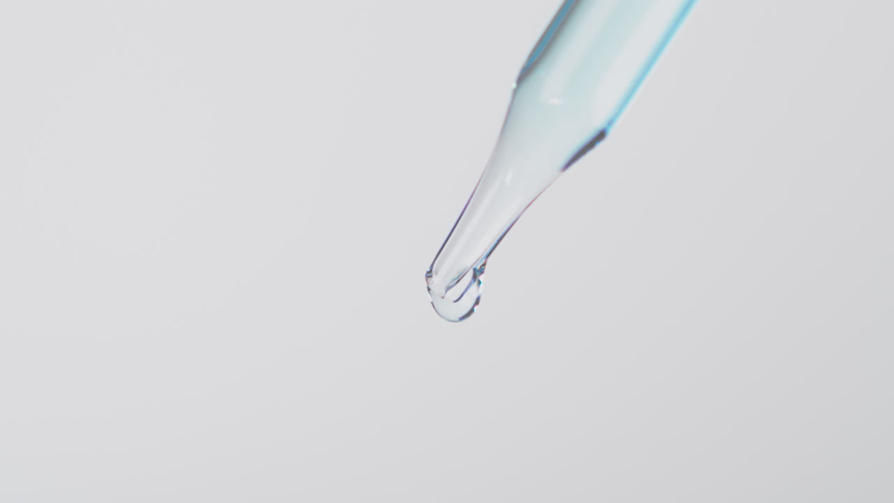 cuentagotas transparente con líquido azul claro colgando en gotas desde el final