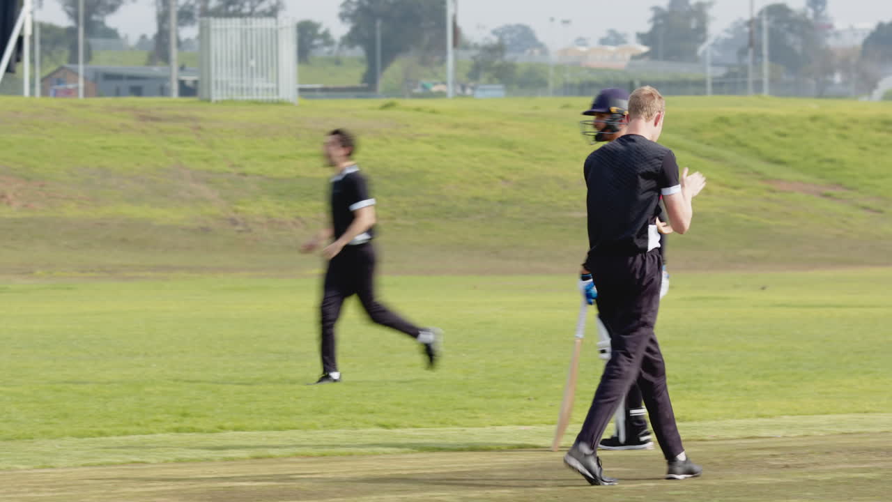 Two teams of multiracial male cricket players playing cricket on pitch
