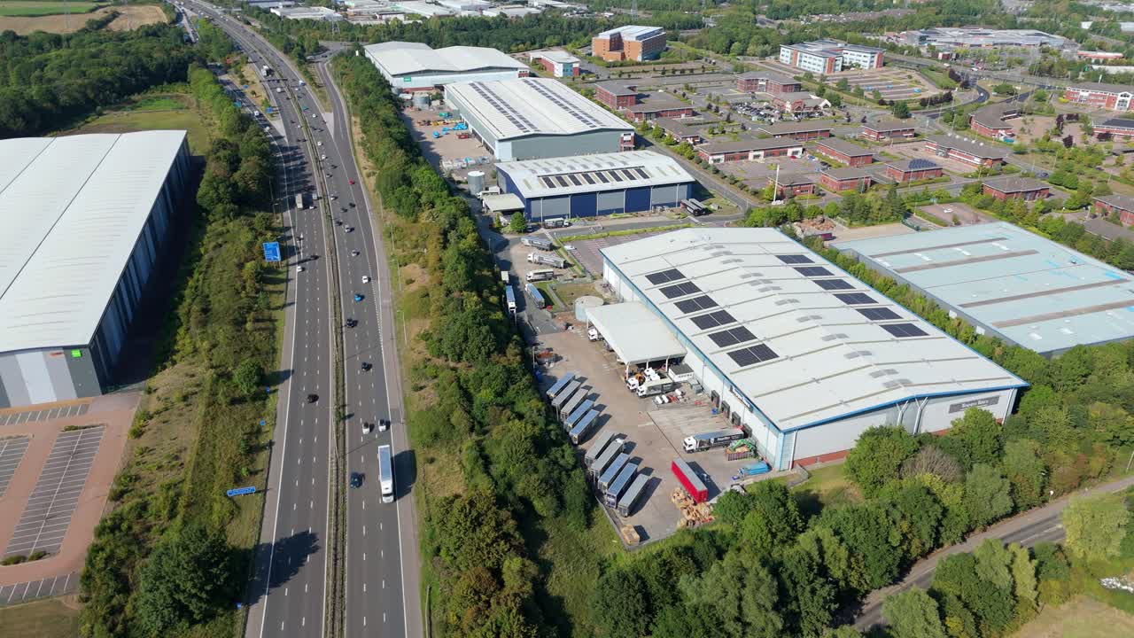 Drone video of large warehouses and factories beside busy M1 highway with cars and trucks in motion at golden hour near Leicester England UK summer