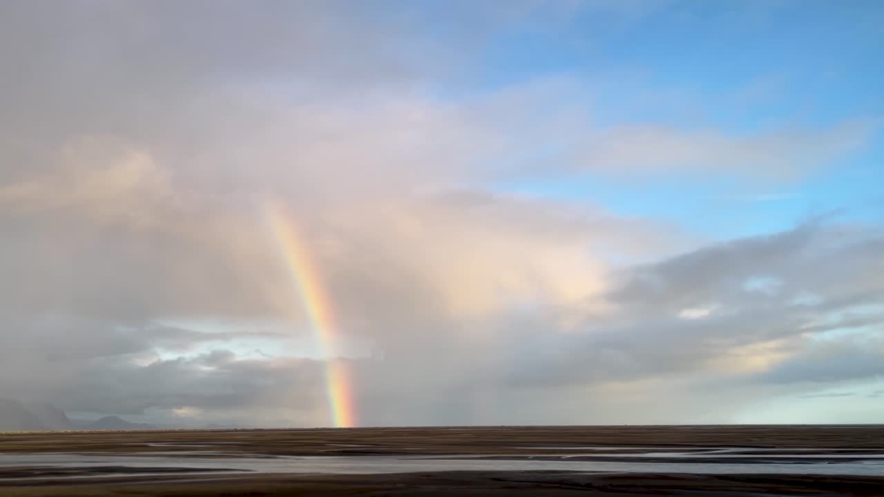 hermoso arco iris por las llanuras islandesas que descienden de la nube a la tierra, desde el coche en movimiento conduciendo por
