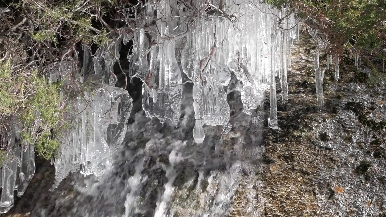 Valle de la Fuenfría, Cercedilla'nın karlı manzaralarında bir şelalenin yanında sarkan buz sarkıtlarını yakalayan yakın çekim bir video.