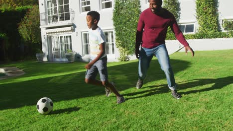 african american dad and son playing football together in the garden on a bright sunny day