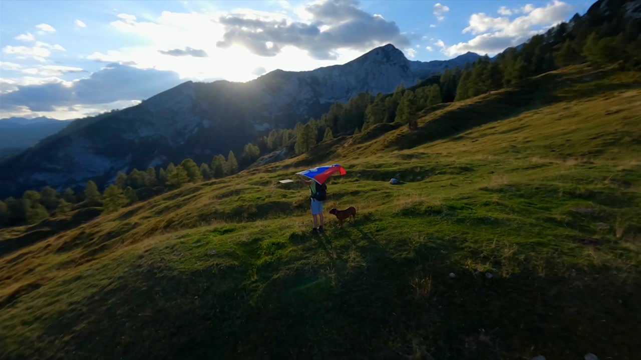 las imágenes de fpv se filmaron en el pueblo de montaña esloveno en los alpes con un dron volando rápido sobre las montañas filmadas con una gopro con increíbles paisajes circundantes con un excursionista sosteniendo una bandera