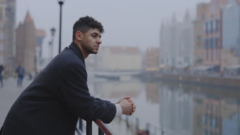 young man contemplating by a city canal on a hazy day