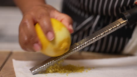 black woman's hands seen zesting a lemon on a grater to use the peel shavings as a tasty ingredient