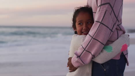 midsection of hispanic mother embracing daughter on beach at sunset