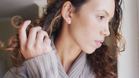 retrato de una mujer biracial pensativa de pie en la ventana y mirando a la distancia