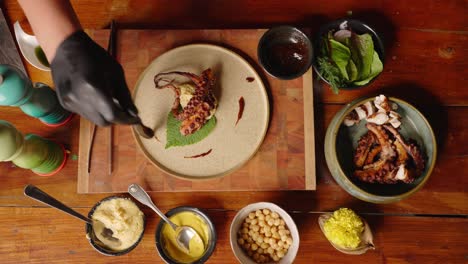 top down view of a sophisticated professional fine dinning chef plating the smoked octopus and drizzle extra virgin olive oil to complete the dish