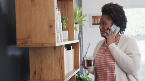 Glückliche-Afroamerikanische-Frau,-Die-Zu-Hause-Tee-Trinkt-Und-Auf-Dem-Smartphone-Spricht