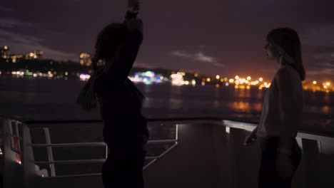 silhouette of two beautiful young women dancing on ship deck at night. girlfriends on the boat