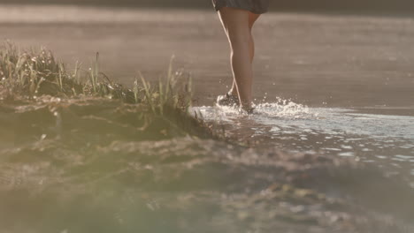 fisherman wades through shallow water, near grassy shoreline in golden light, captured in slow motion